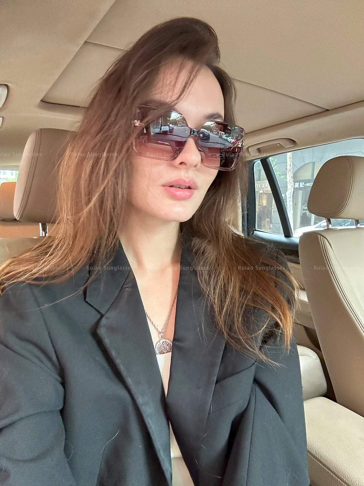 Woman wearing sunglasses and a dark blazer inside a car.