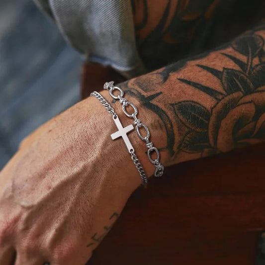 Silver chain bracelet with a cross on a tattooed arm.