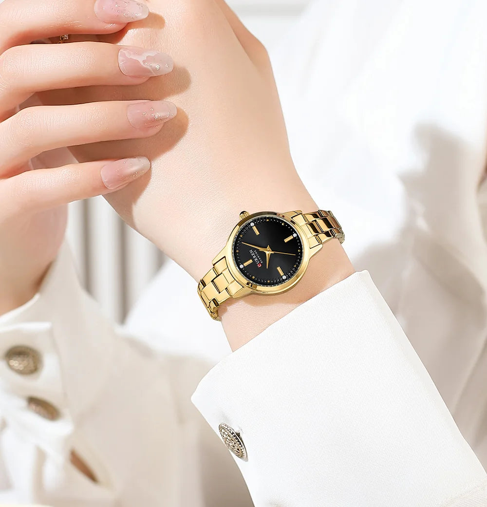 Gold wristwatch with black face on a person's wrist against a white background