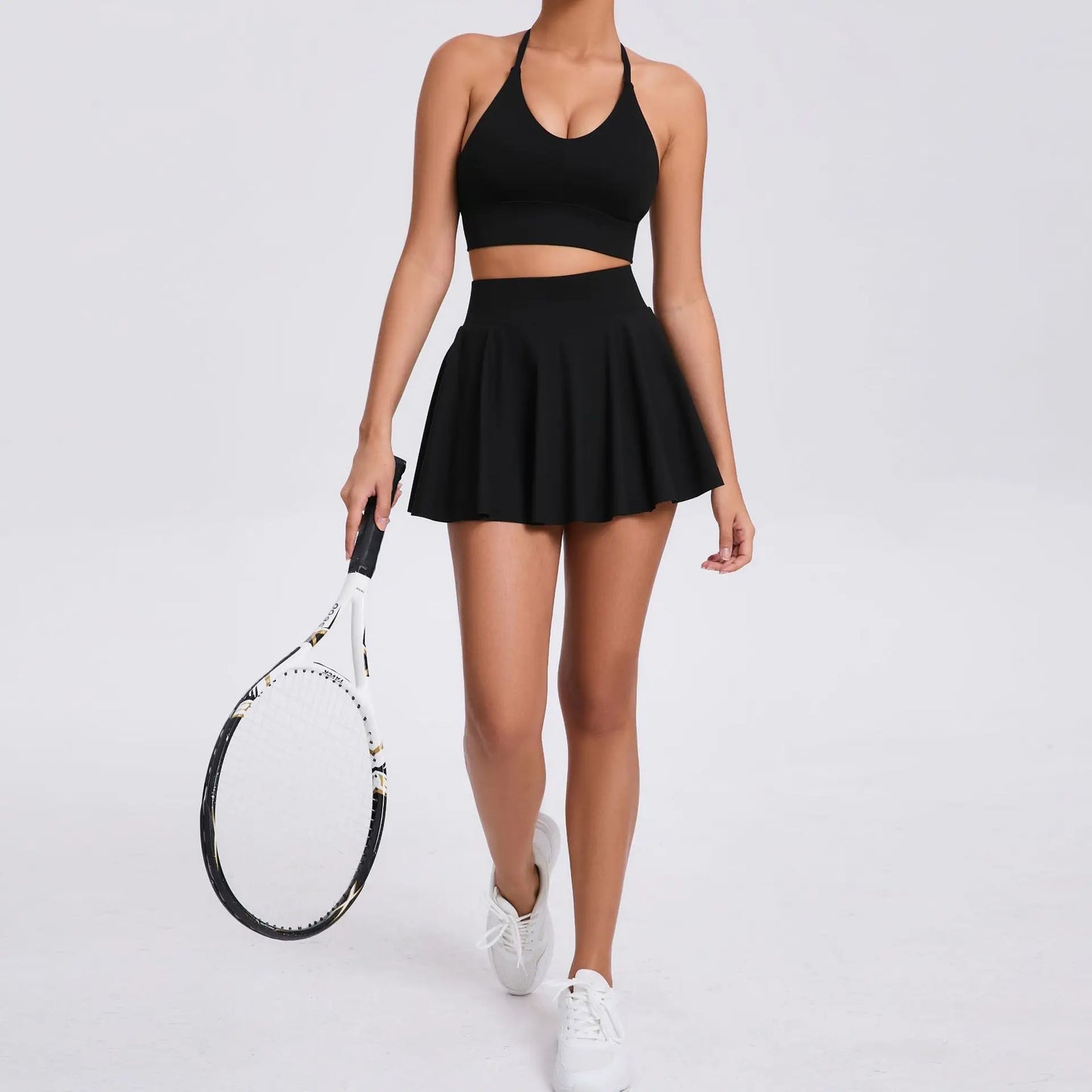 Person wearing a black athletic outfit holding a tennis racket on a light gray background