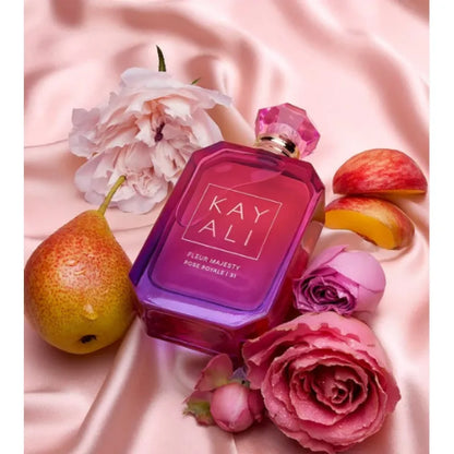 Pink perfume bottle labeled 'KAY ALI' surrounded by flowers and fruits on a pink fabric background