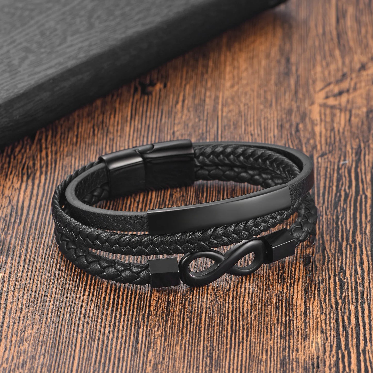 Black braided leather bracelet with metal clasp on a wooden surface