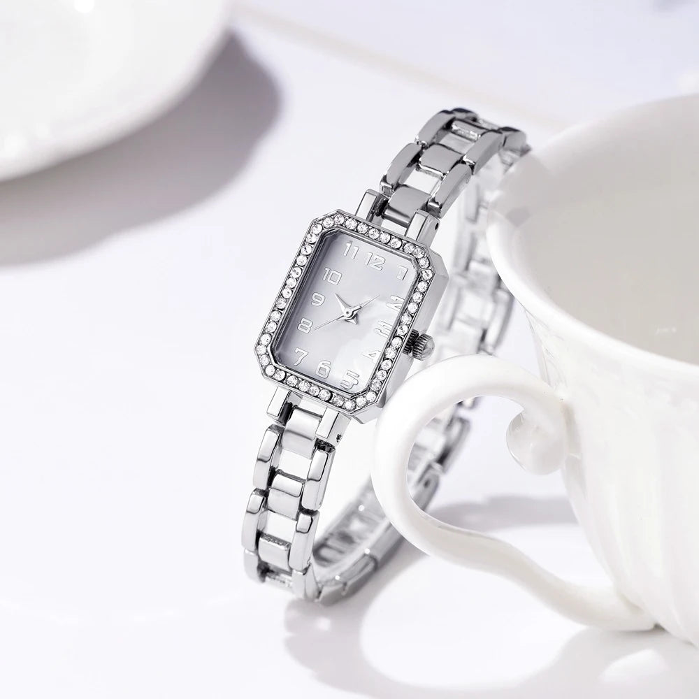 Silver wristwatch with a white face on a white surface with a blurred background