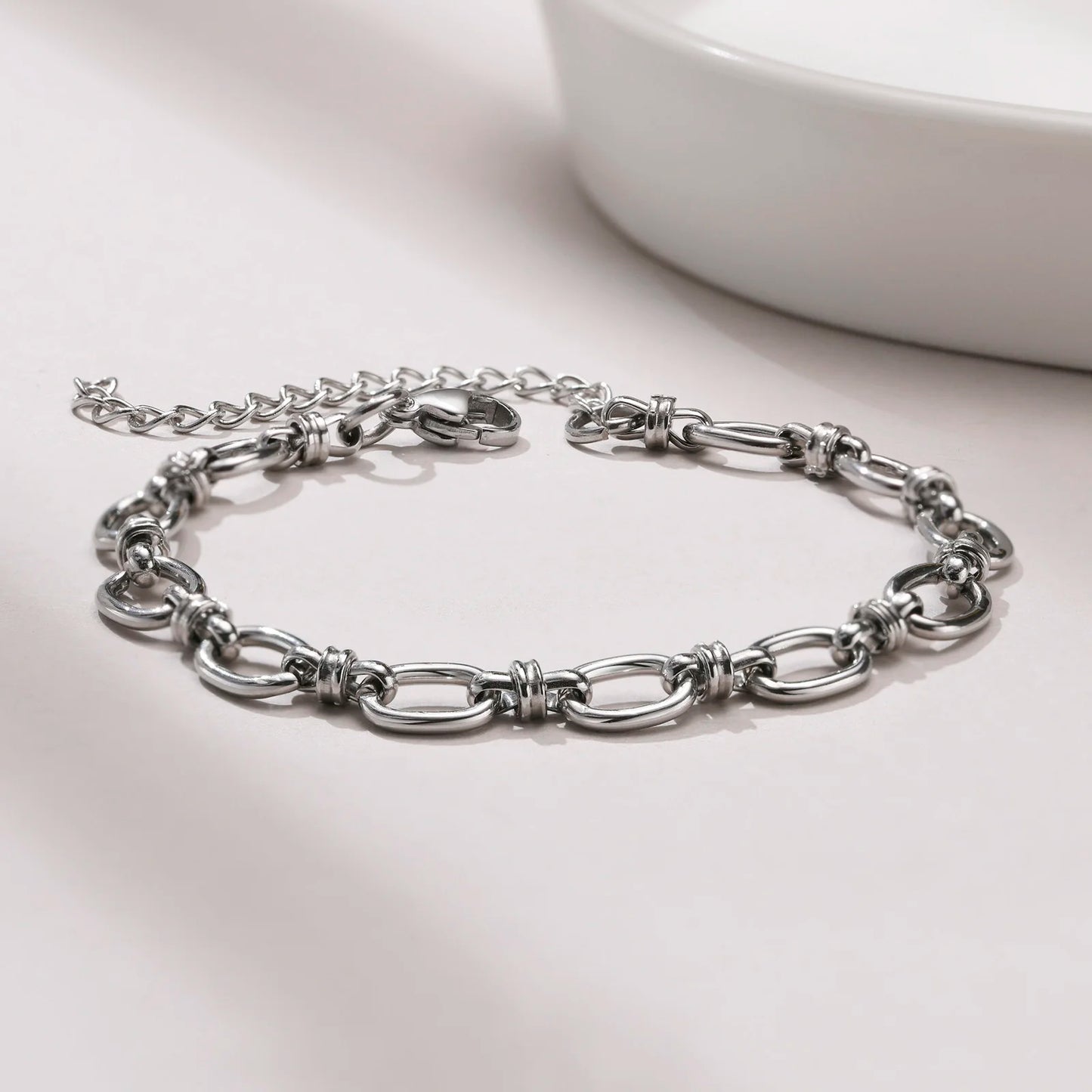 Silver chain bracelet on a light gray surface with a white bowl in the background
