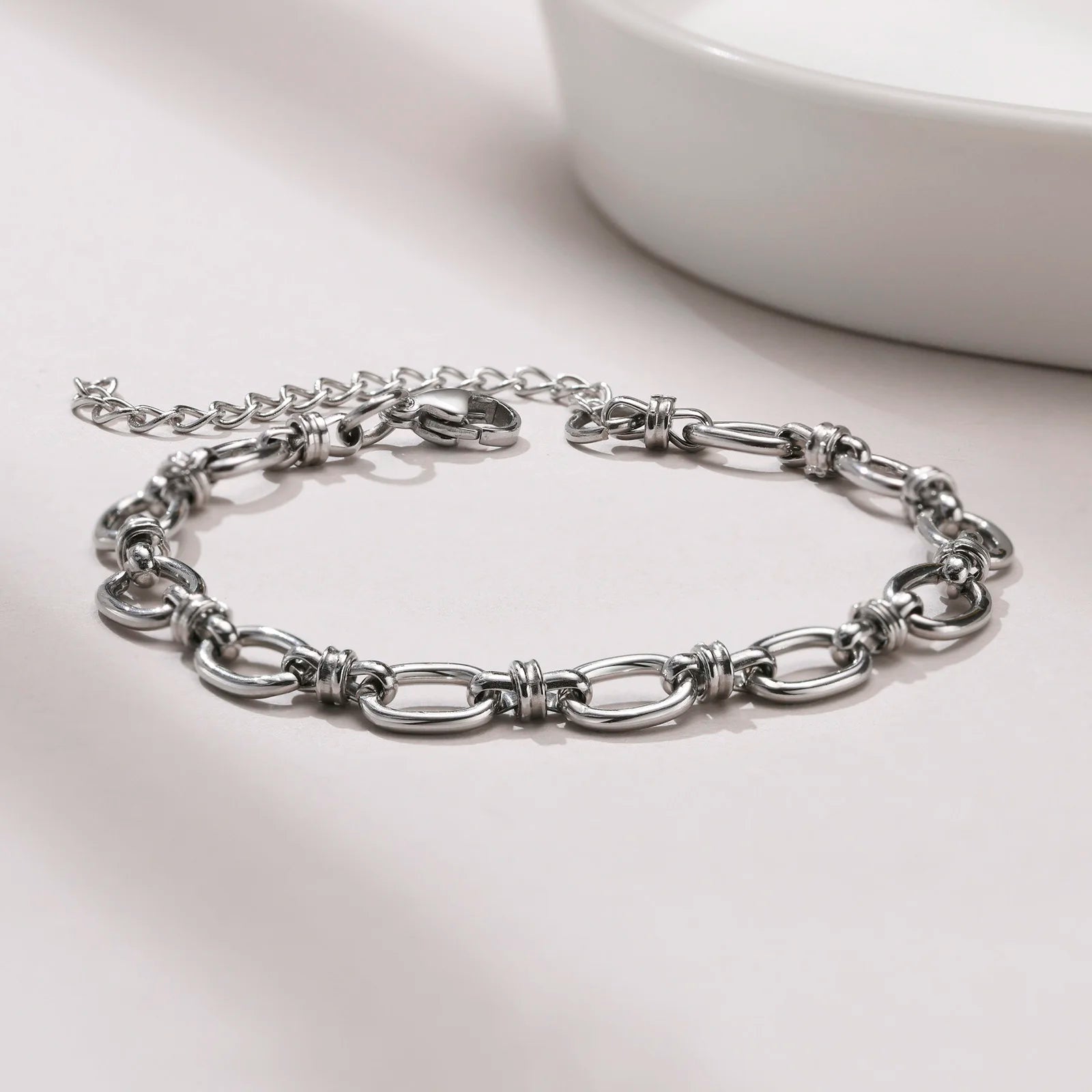 Silver chain bracelet on a light gray surface with a white bowl in the background