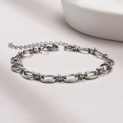 Silver chain bracelet on a light gray surface with a white bowl in the background