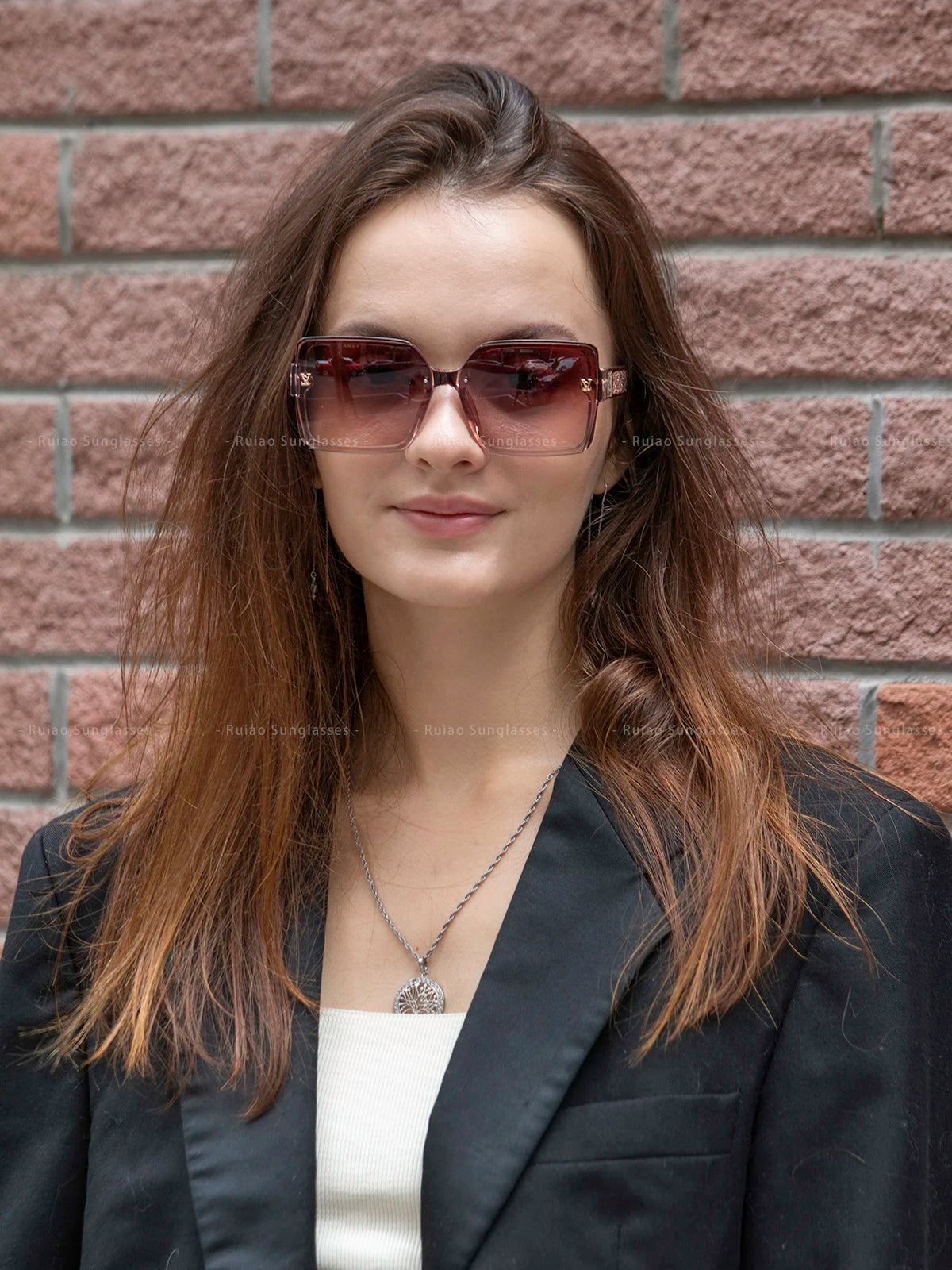 Woman wearing sunglasses and a black blazer against a brick wall