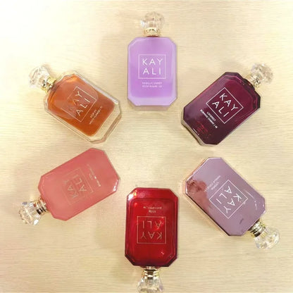 Collection of Kay Ali perfume bottles in various colors on a light wooden surface.