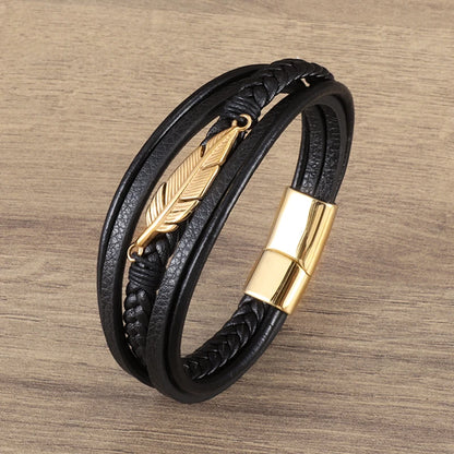 Black leather bracelet with gold feather charm and clasp on a wooden surface