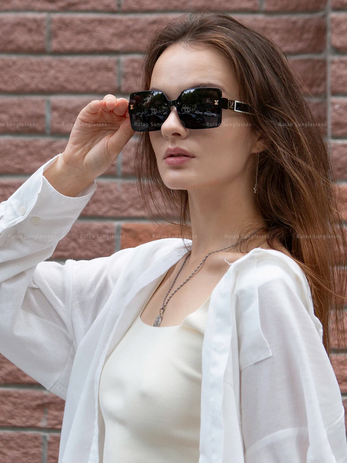 Woman wearing sunglasses with a white shirt against a brick wall