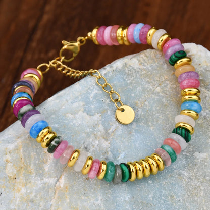 Multicolored beaded bracelet with gold accents on a textured stone surface