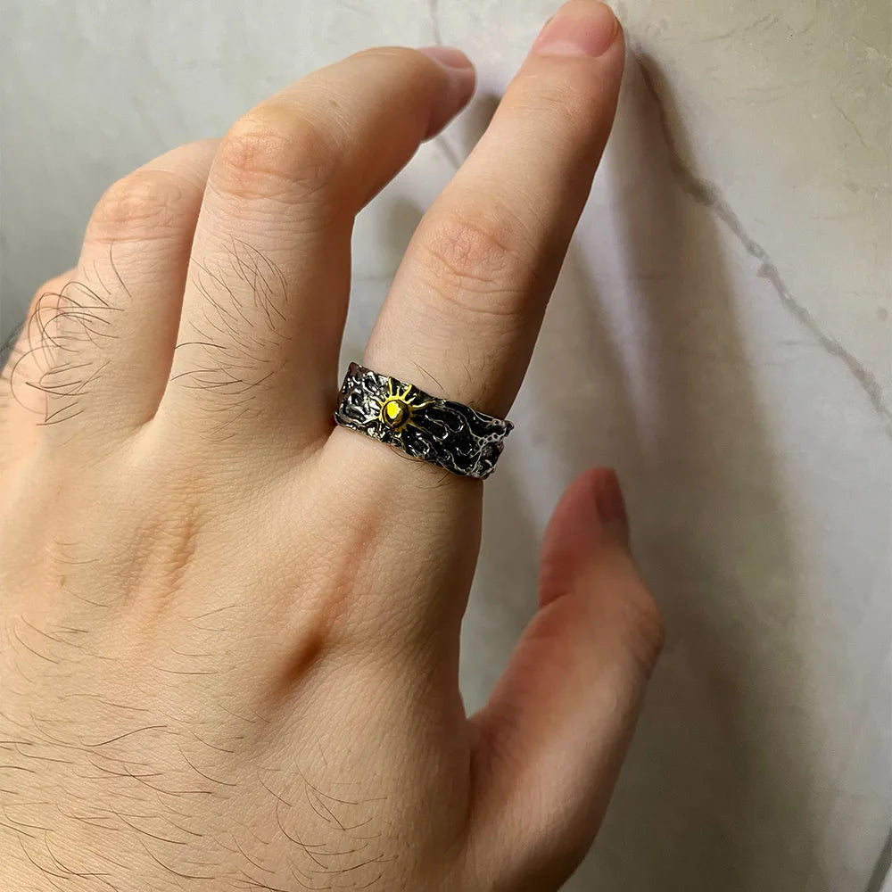 Hand wearing a black chain ring with a yellow gemstone on a light background