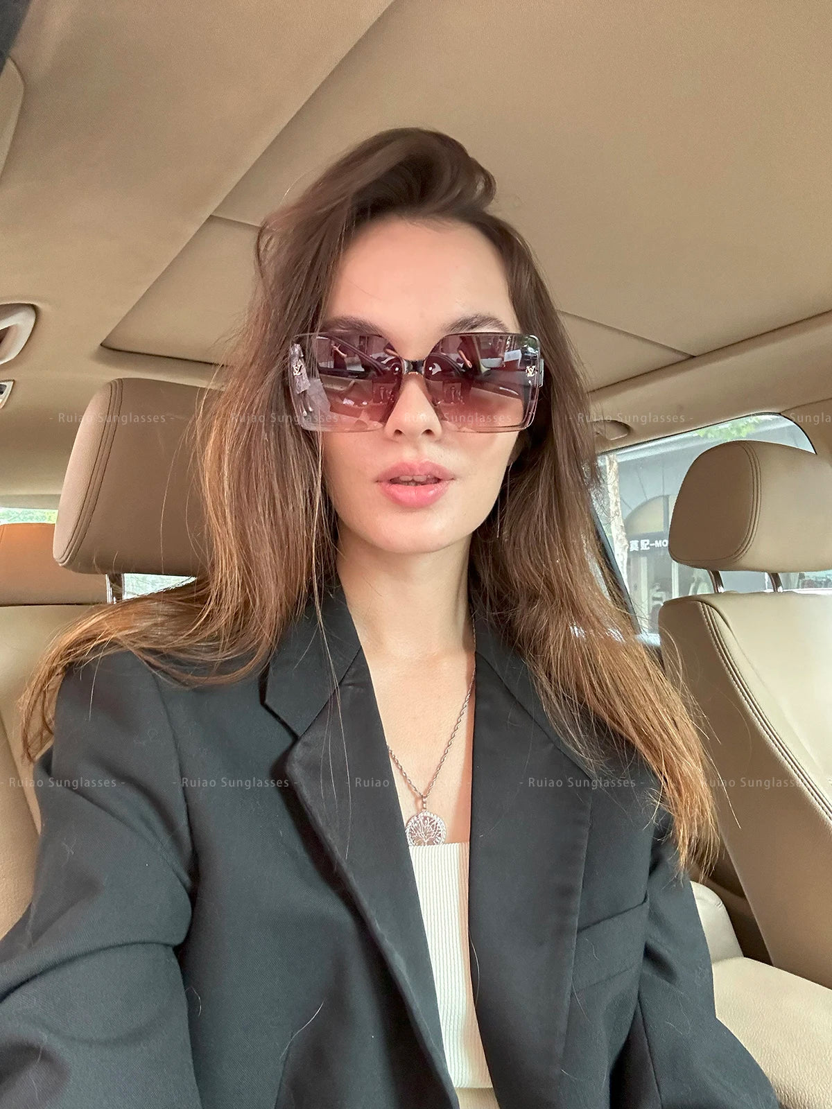Woman wearing sunglasses and a dark blazer inside a car.
