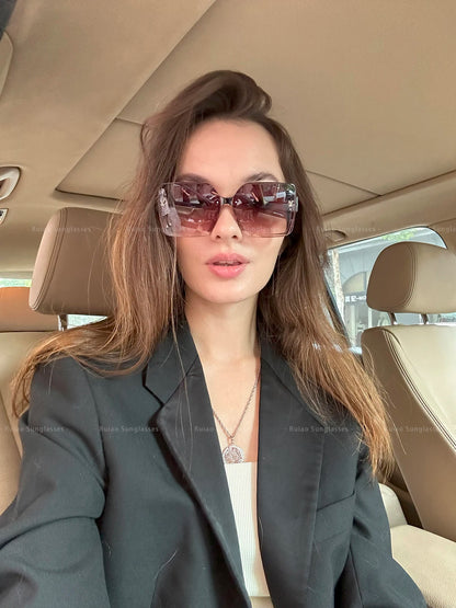Woman wearing sunglasses and a dark blazer inside a car.