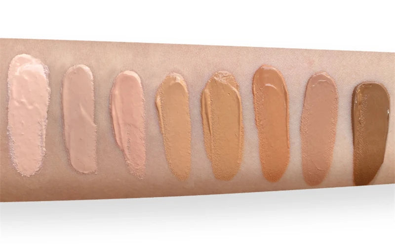 Swatches of different beige and brown makeup products on a skin-toned arm.