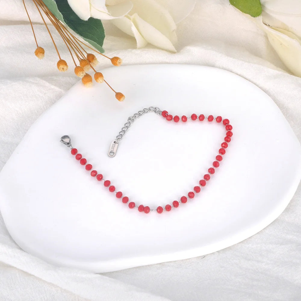 Red beaded necklace on a white dish with flowers in the background