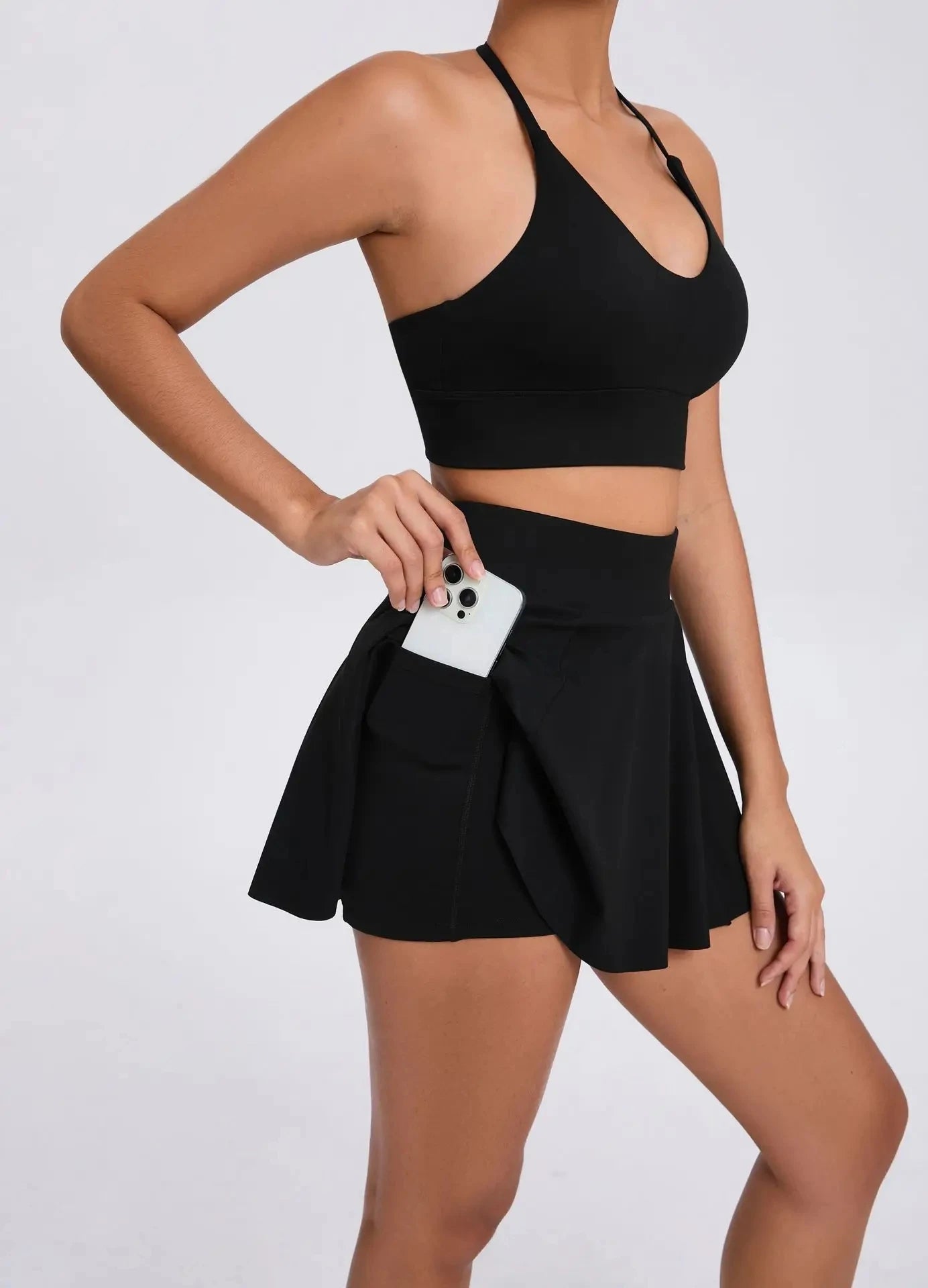 Person wearing a black sports bra and skirt holding a phone on a white background