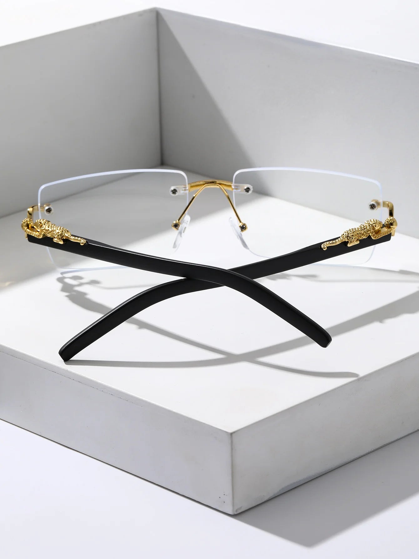 Two pairs of eyeglasses with gold and black frames on a white surface.