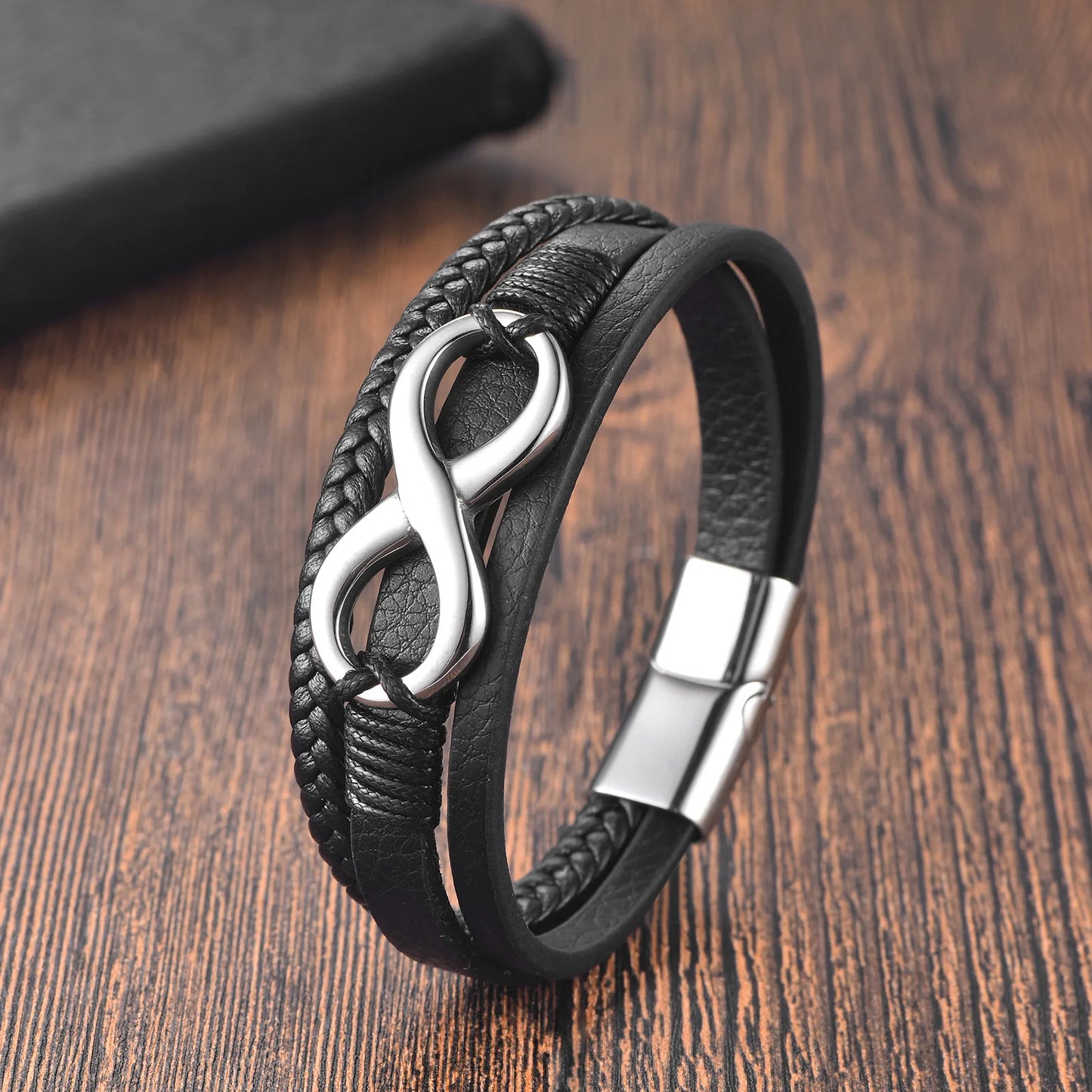 Black braided leather bracelet with silver infinity symbol on a wooden surface