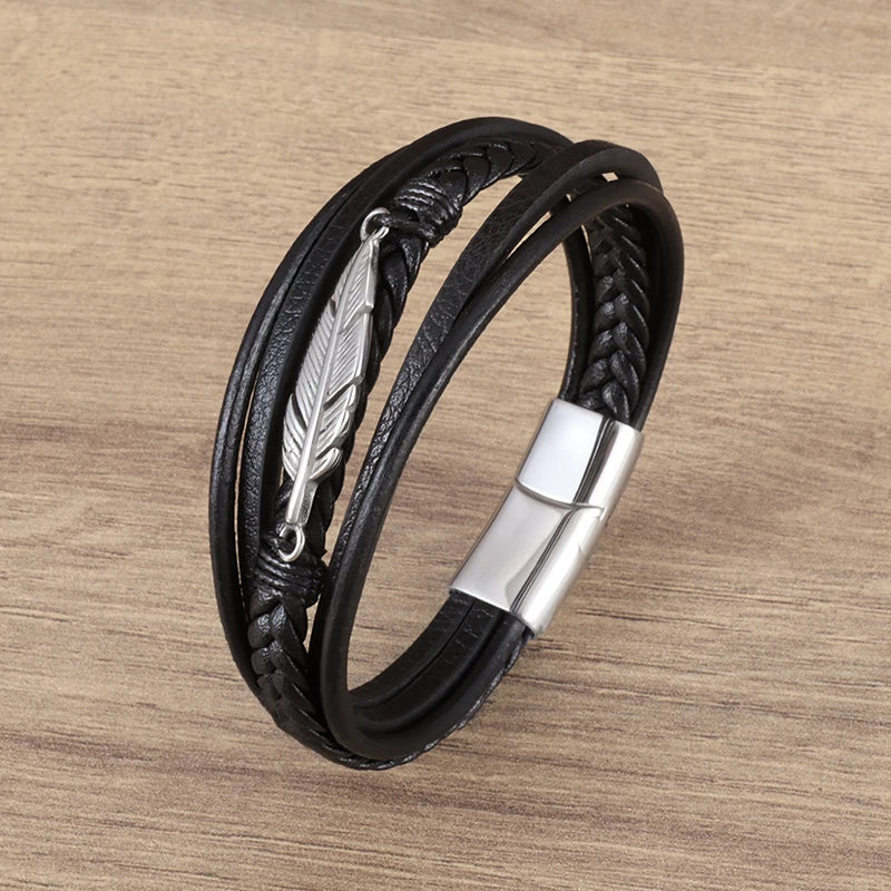 Black leather bracelet with silver feather charm on a wooden surface