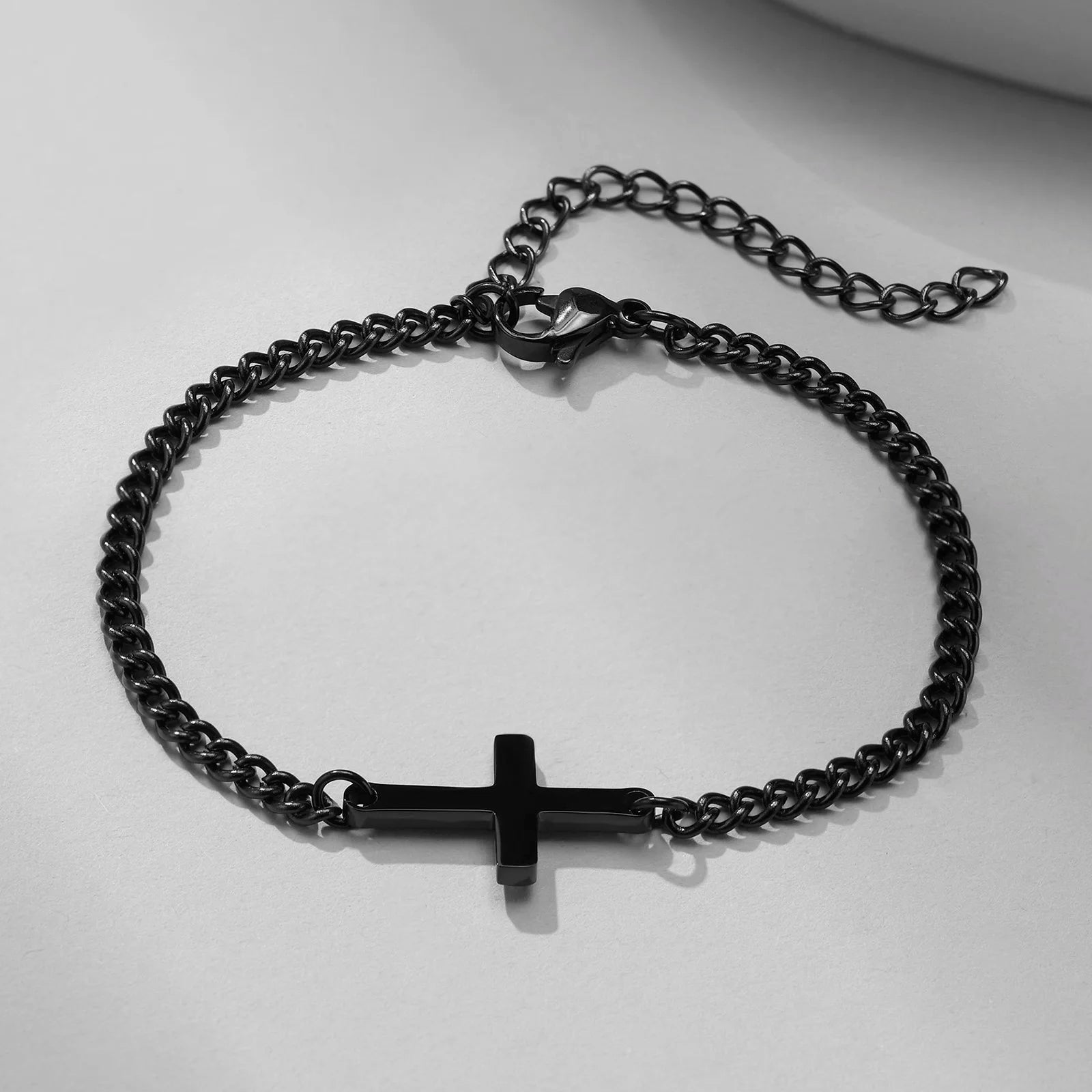 Black chain bracelet with a cross pendant on a light gray background