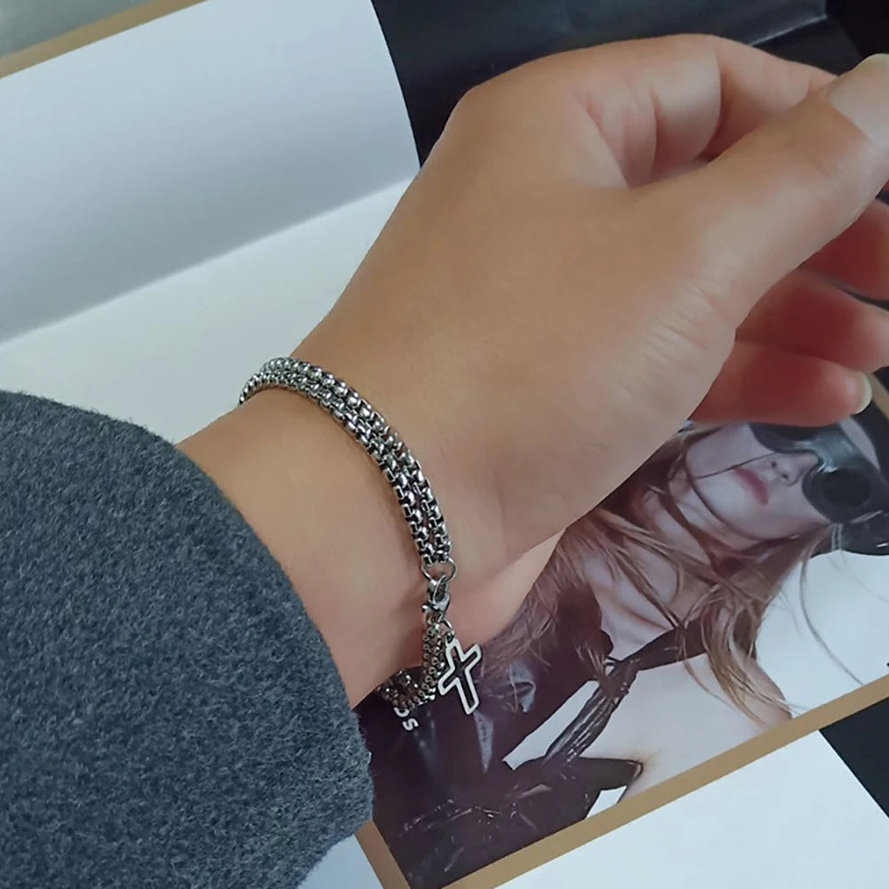 Hand wearing a silver bracelet with a cross charm on a magazine background