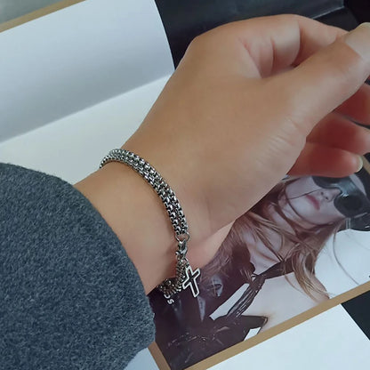 Hand wearing a silver bracelet with a cross charm on a magazine background