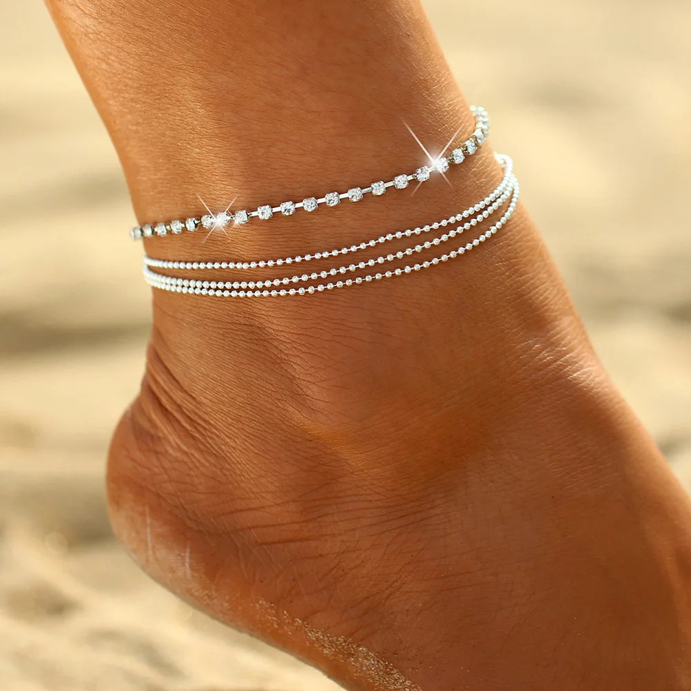 Silver anklets on a person's ankle with a blurred sand background