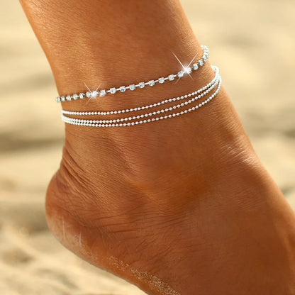 Silver anklets on a person's ankle with a blurred sand background