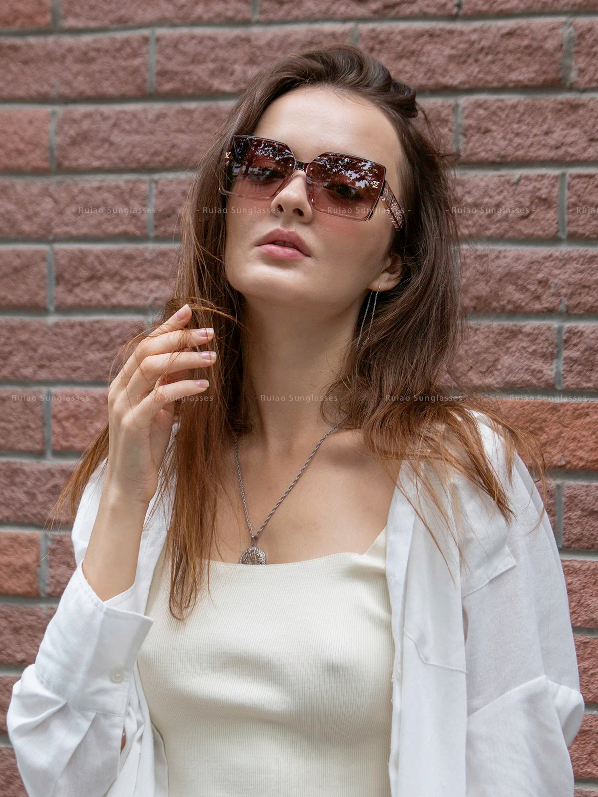 Woman wearing sunglasses and a white outfit against a brick wall