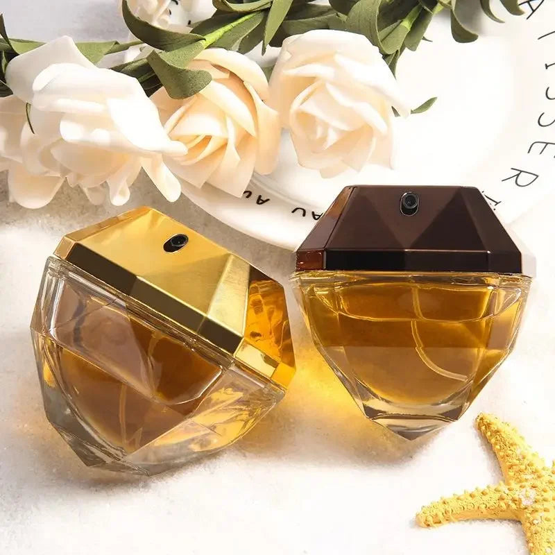 Two perfume bottles with gold caps on a white surface with flowers in the background