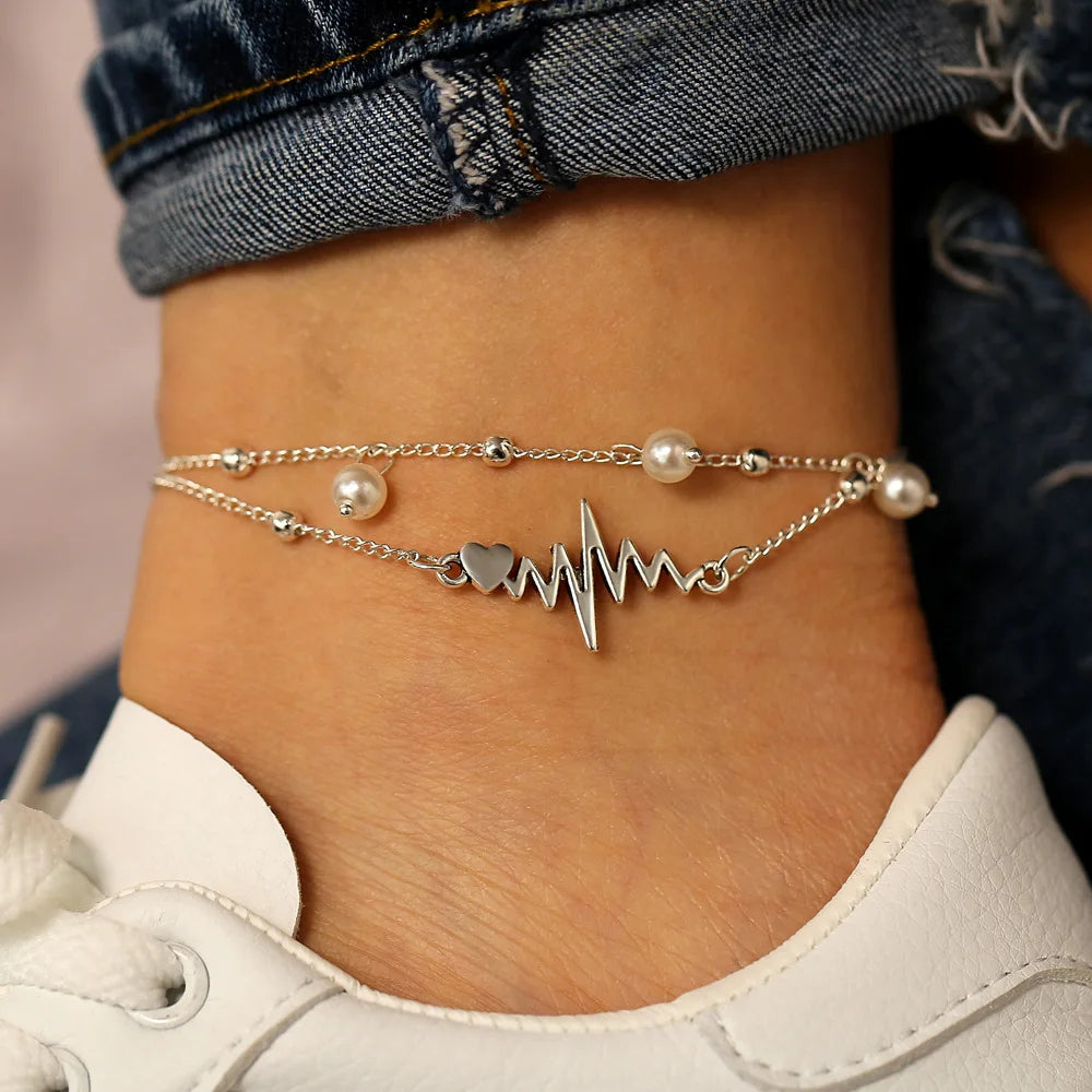 Ankle bracelet with heart rate design and pearl beads on a person wearing jeans and white sneakers.