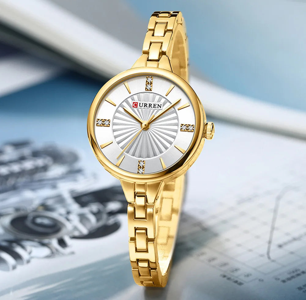 Gold wristwatch with a white face on a blurred background