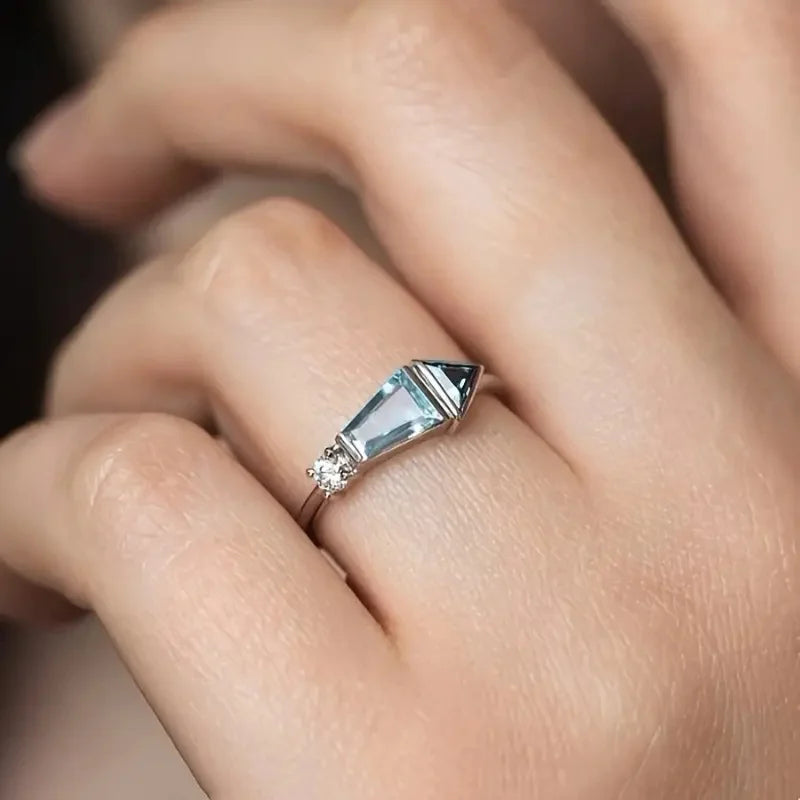 Close-up of a hand wearing a ring with a clear gemstone on a blurred background