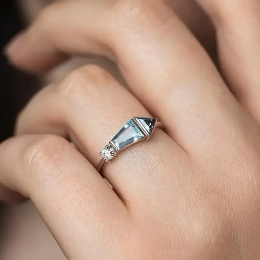 Close-up of a hand wearing a ring with a clear gemstone on a blurred background