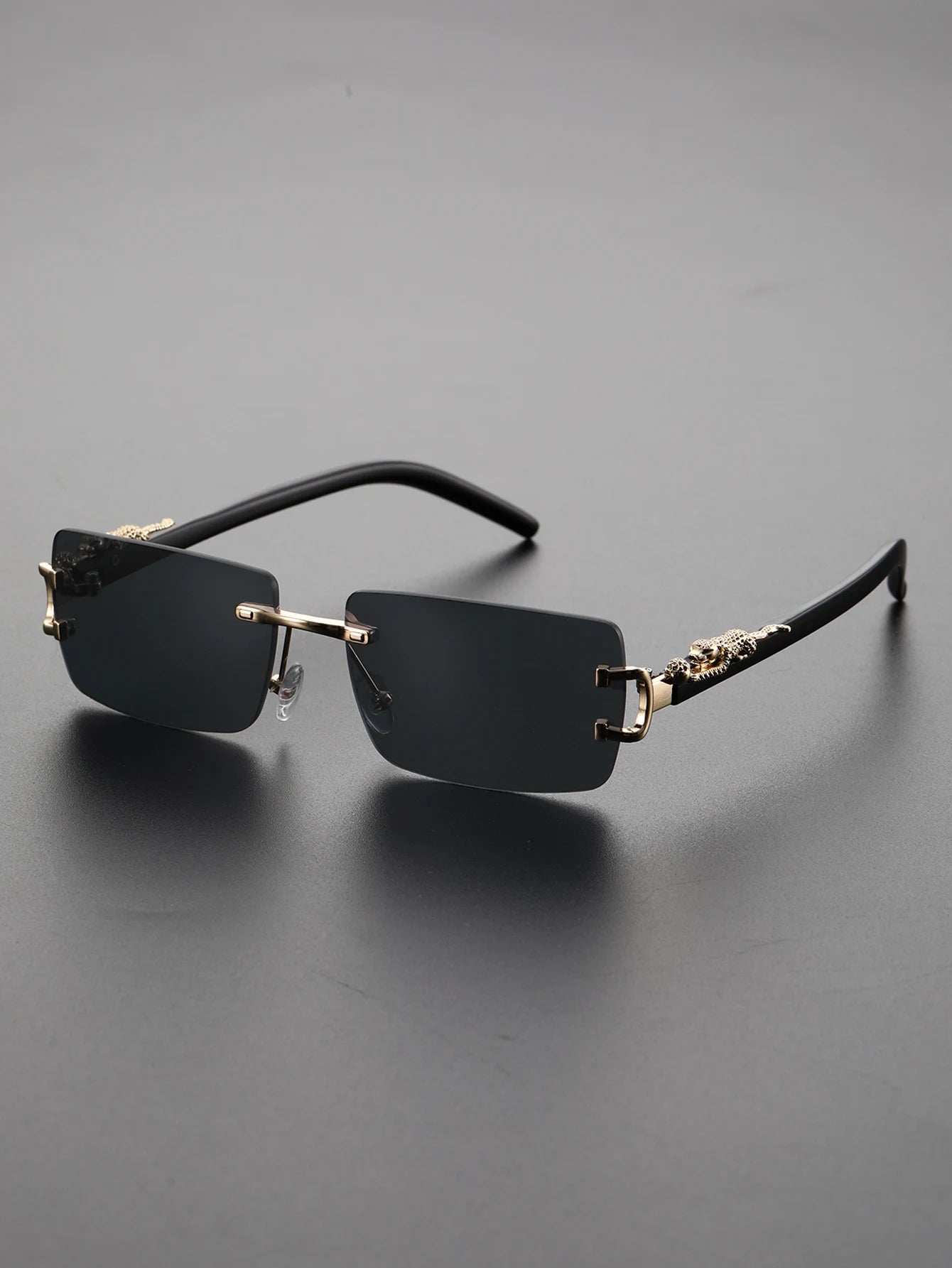 Black rimless sunglasses with gold accents on a gray background