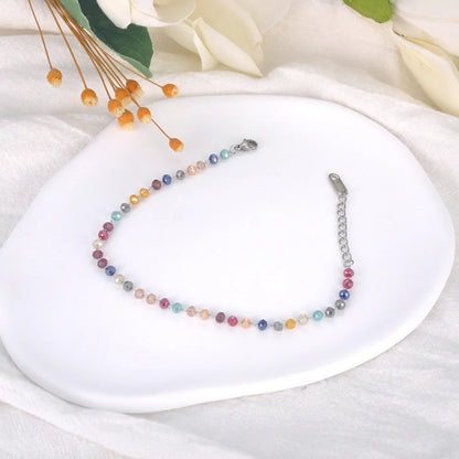 Multicolored beaded necklace on a white plate with flowers in the background