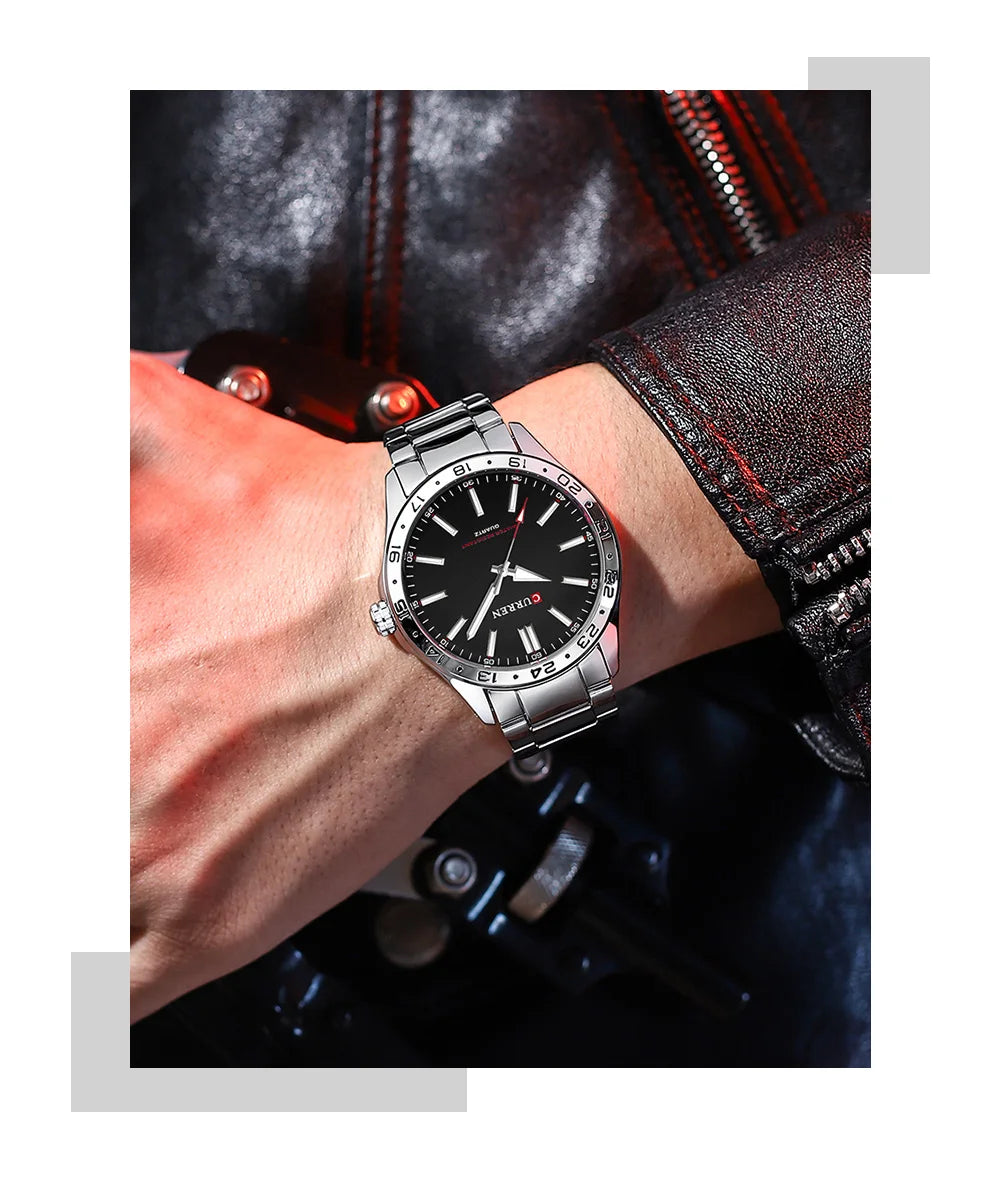 Silver watch with black dial on a wrist, worn against a dark jacket.