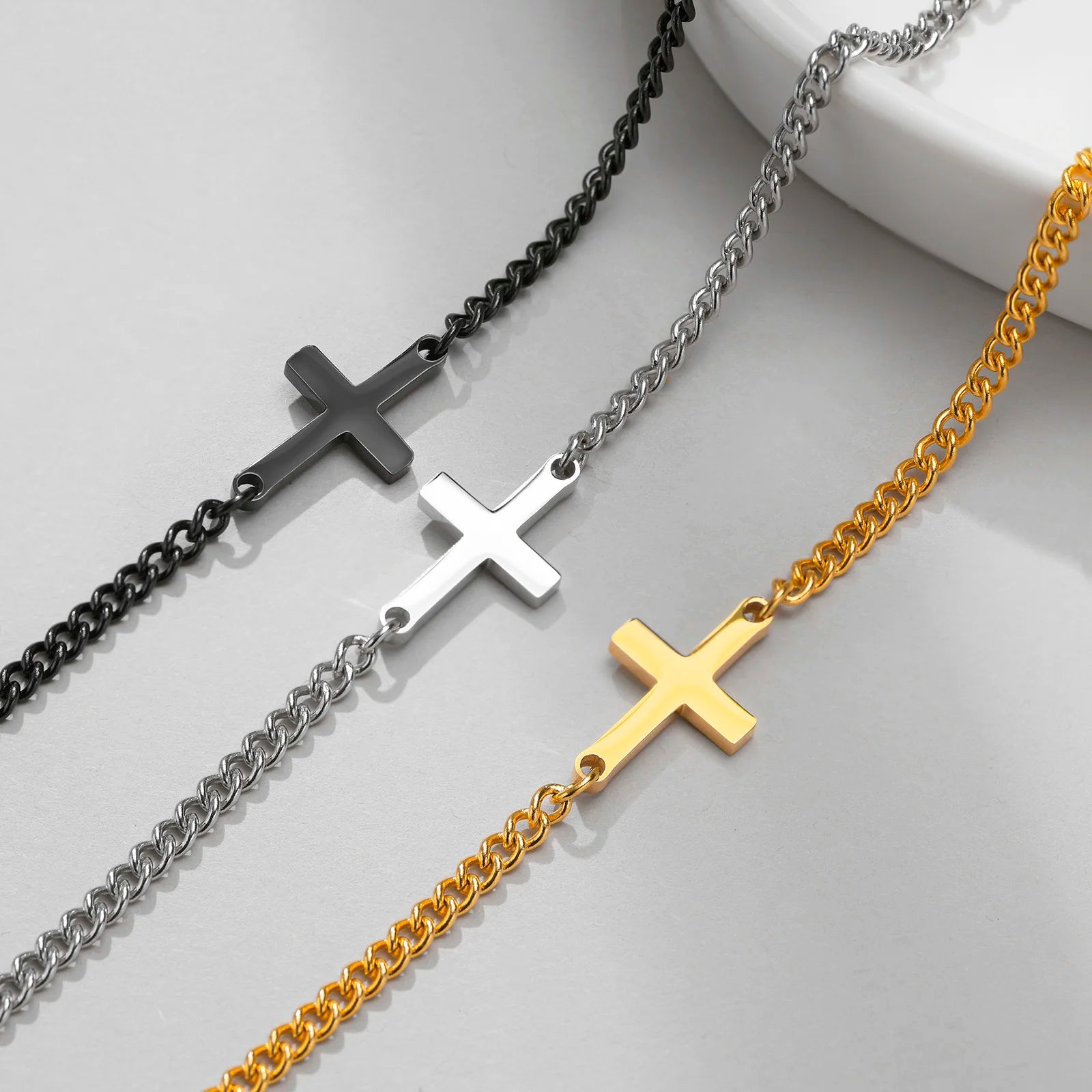 Four cross-shaped pendants on chains in black, silver, and gold on a light gray background.