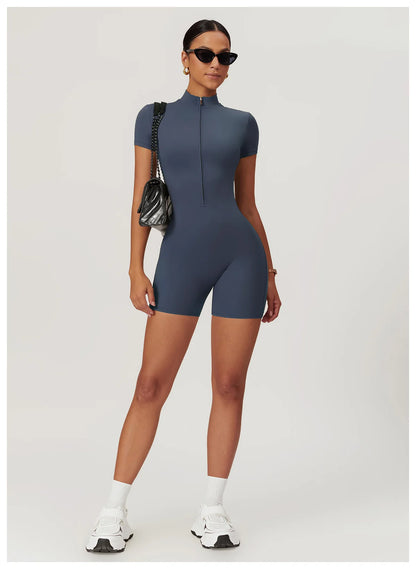 Woman wearing a blue bodysuit with sunglasses and a black handbag on a white background