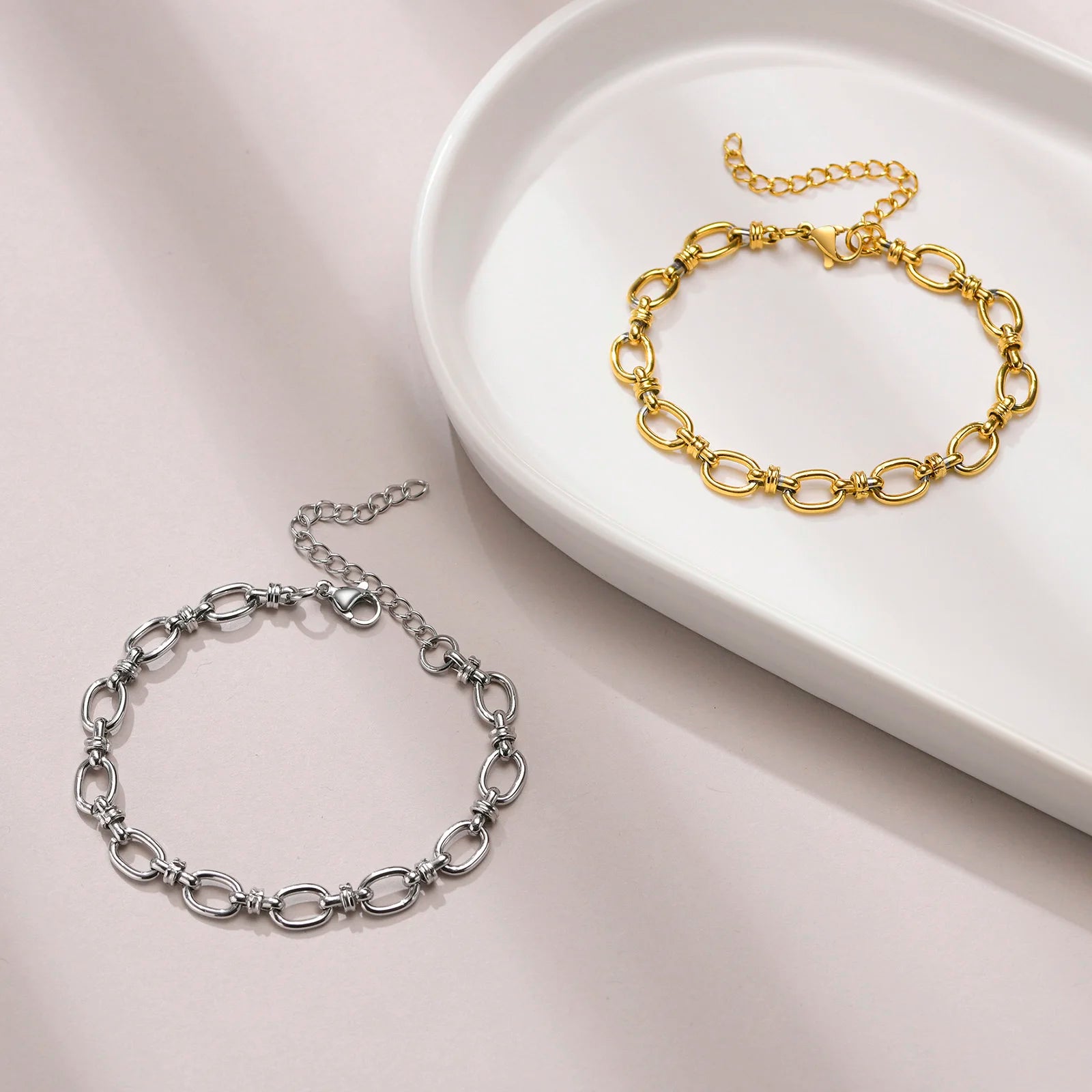 Gold and silver chain bracelets on a white dish with a light pink background