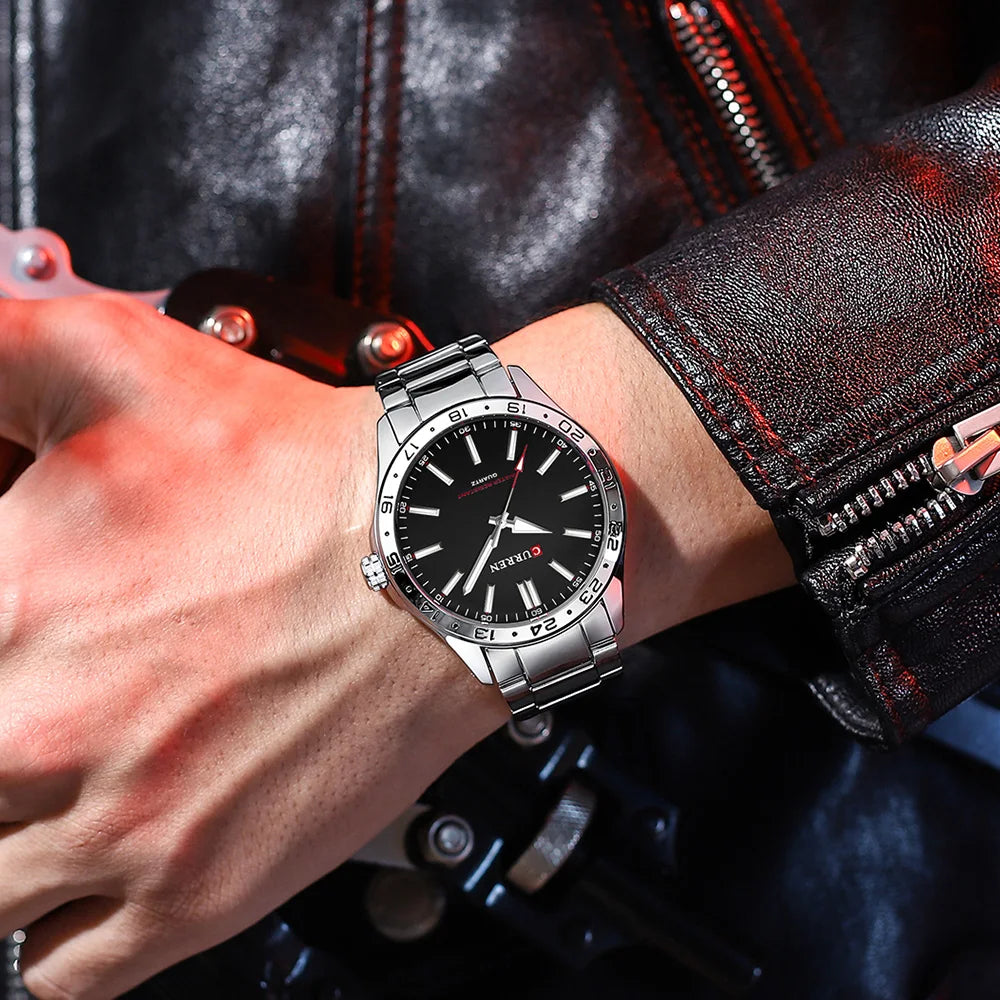 Close-up of a wrist wearing a silver watch with a black face, against a dark background.