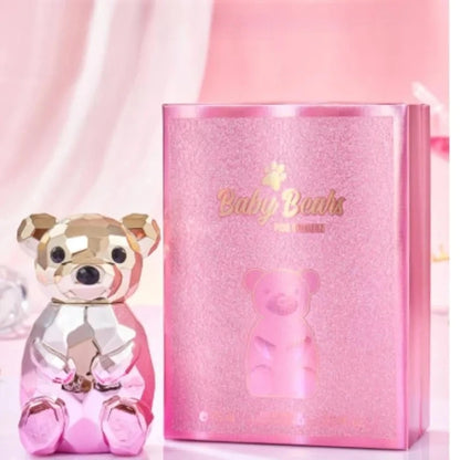 Pink teddy bear figurine next to its packaging on a pink background