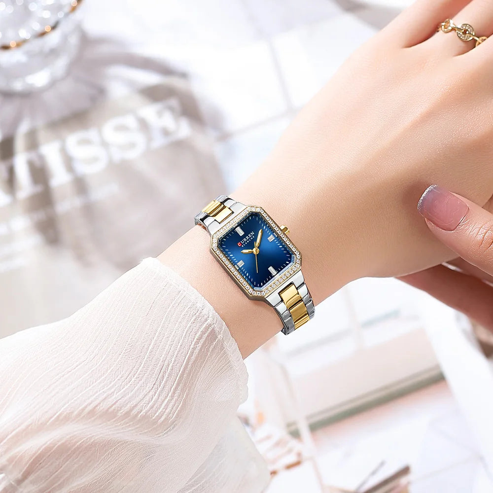 Gold and silver watch with blue face on a wrist against a blurred background