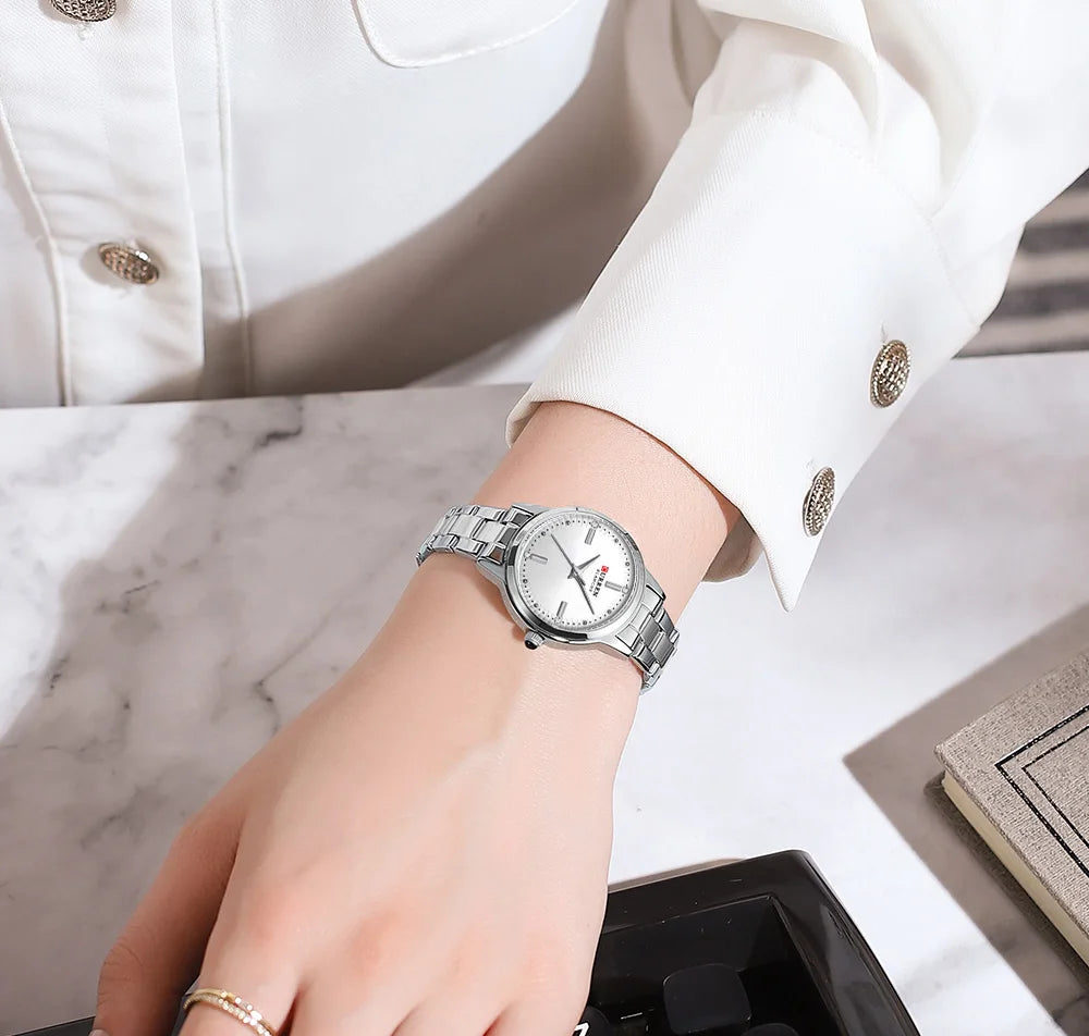 Silver watch on a wrist with a white jacket and marble surface in the background