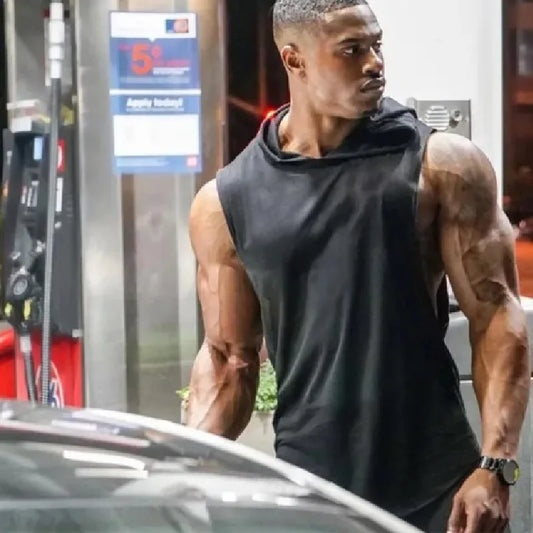 Man in a black sleeveless shirt standing next to a car at a gas station.