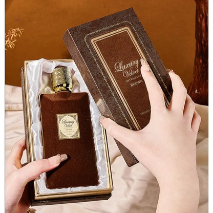 Brown perfume bottle with velvet packaging held by hands against a brown background