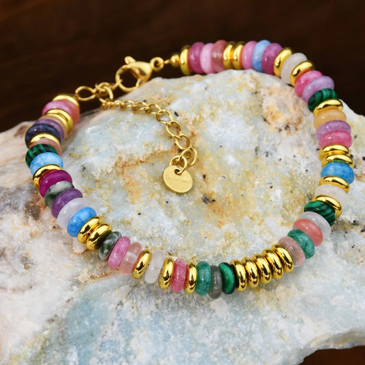Multicolored beaded bracelet with gold accents on a textured stone surface