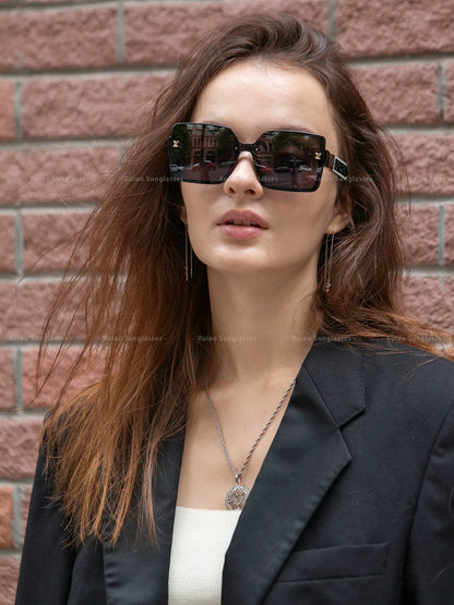 Woman wearing sunglasses and a black blazer against a brick wall