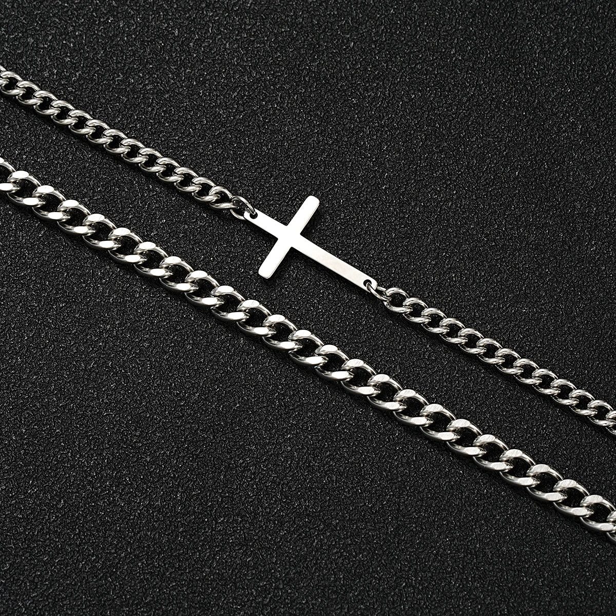 Two necklaces on a black background, one with a silver cross pendant and the other with a thick chain.